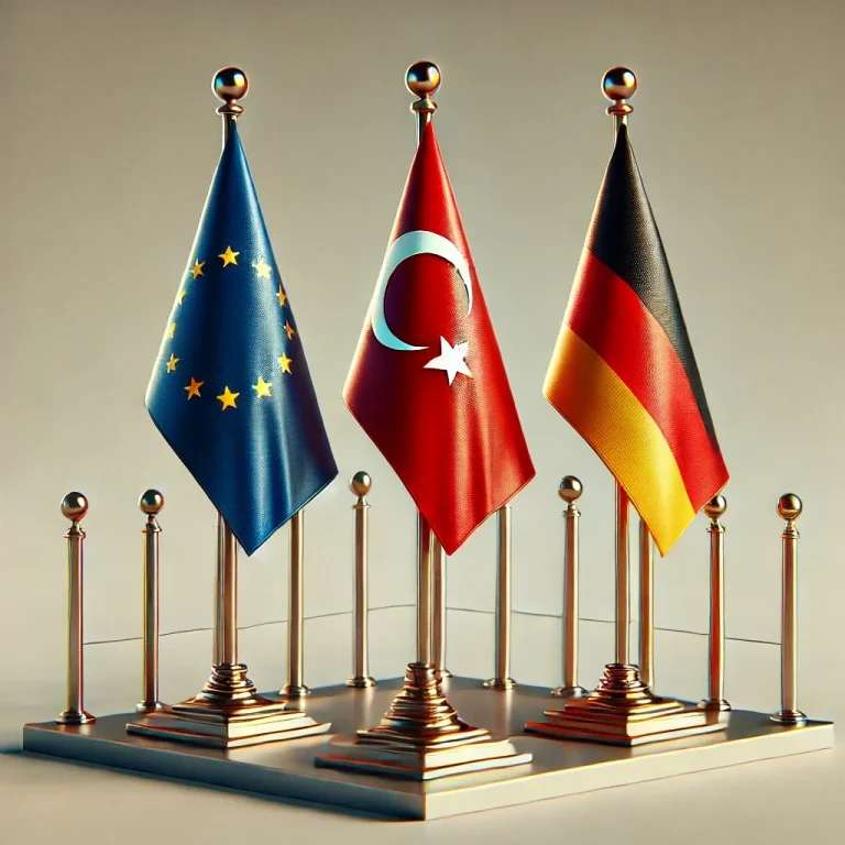 Drei Fahnen: EU, Türkei und Deutschland, auf einem Sockel mit goldenen Ständern.